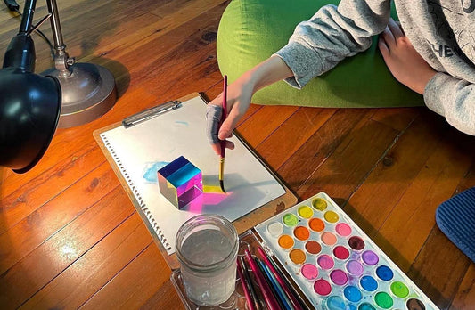 Child painting a watercolour picture of a CMY Cube