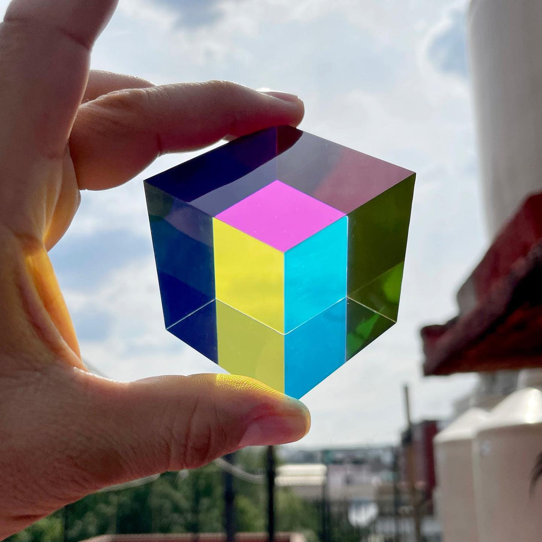 Fingers holding the Original CMY Cube up to the sky outdoors