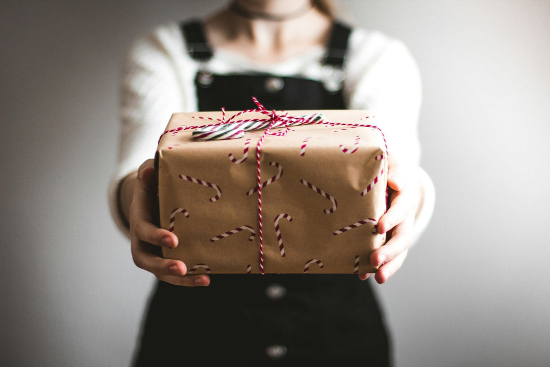 Hands holding out a Christmas gift wrapped in brown paper with a candy cane pattern and red and white twine