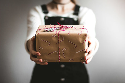 Hands holding out a Christmas gift wrapped in brown paper with a candy cane pattern and red and white twine